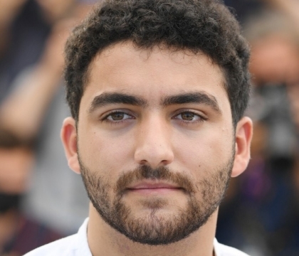 A man with dark hair, a beard, and a white shirt