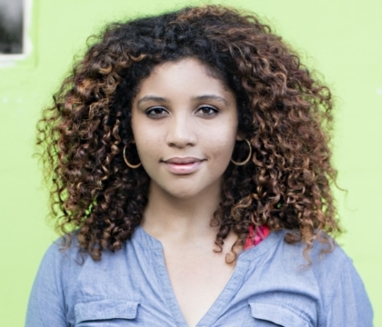 Woman wearing blue button-up facing camera in front of green background