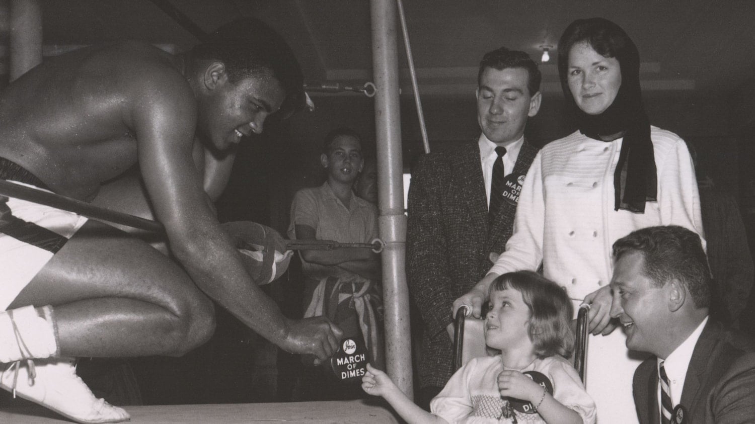 A boxer leans out of the ring to hand a pin to a child in a wheelchair