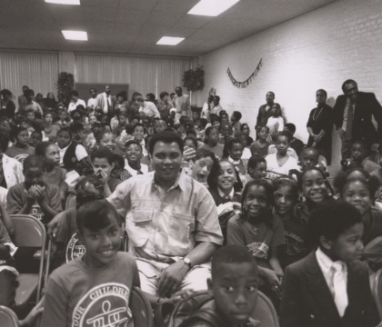 Black and white photo of Muhammad Ali sitting in a room full of students