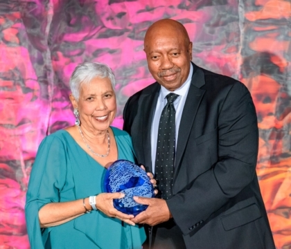 A woman in a dress and a man in a suit posing with a large blue award trophy