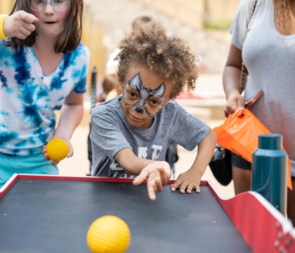 Boy rolls ball in carnival game while girl cheers him on