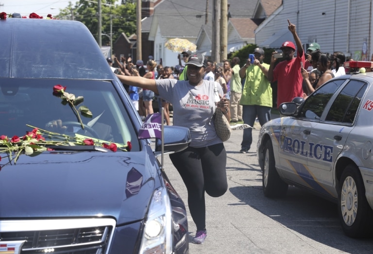 Woman in gray t-shirt runs alongside a hearse