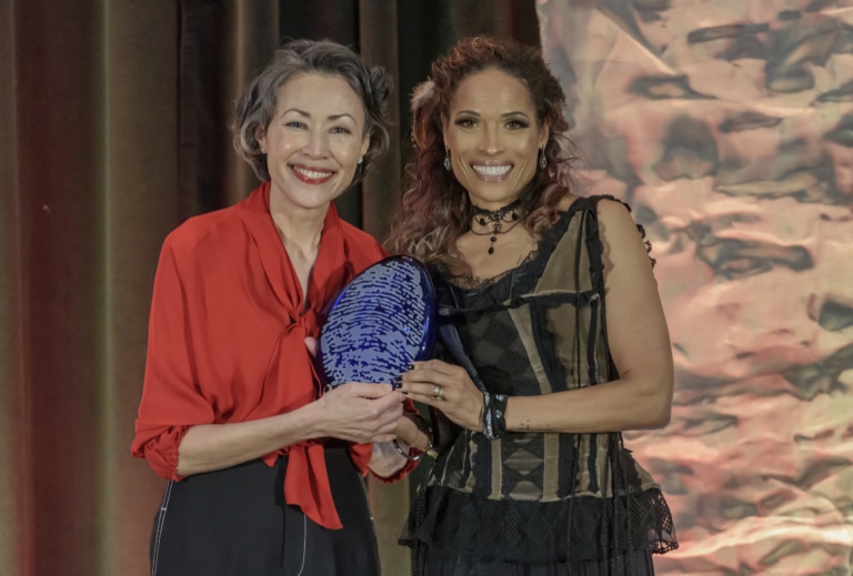 Two women posing for camera while holding an award