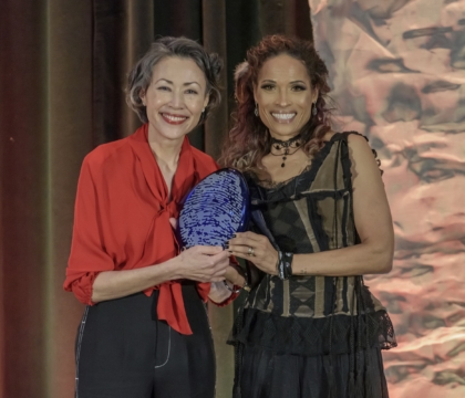 Two women posing for camera while holding an award