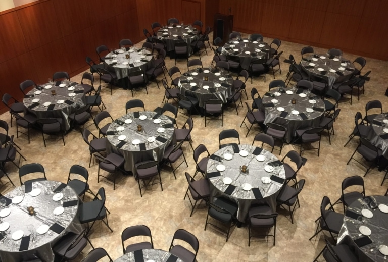 Room with large round banquet tables and folding chairs set up for an event