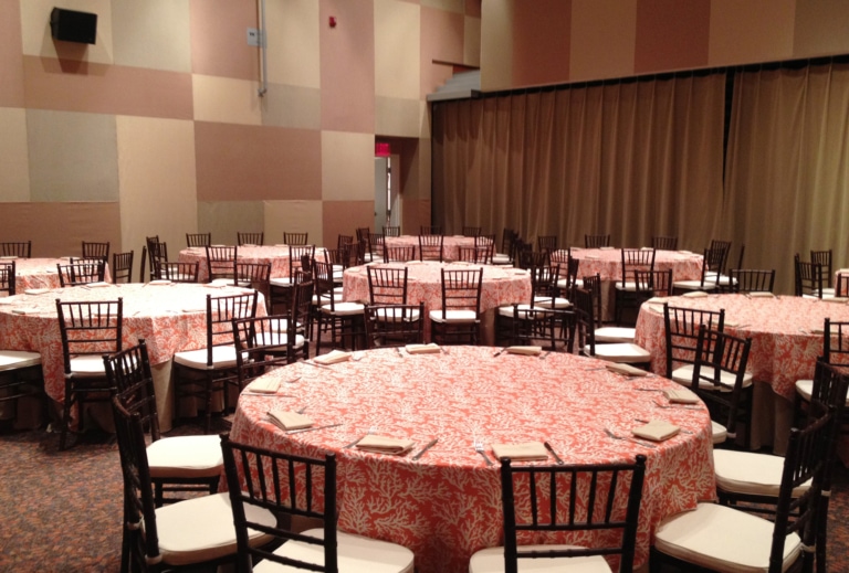 Room with large round banquet tables and folding chairs set up for an event