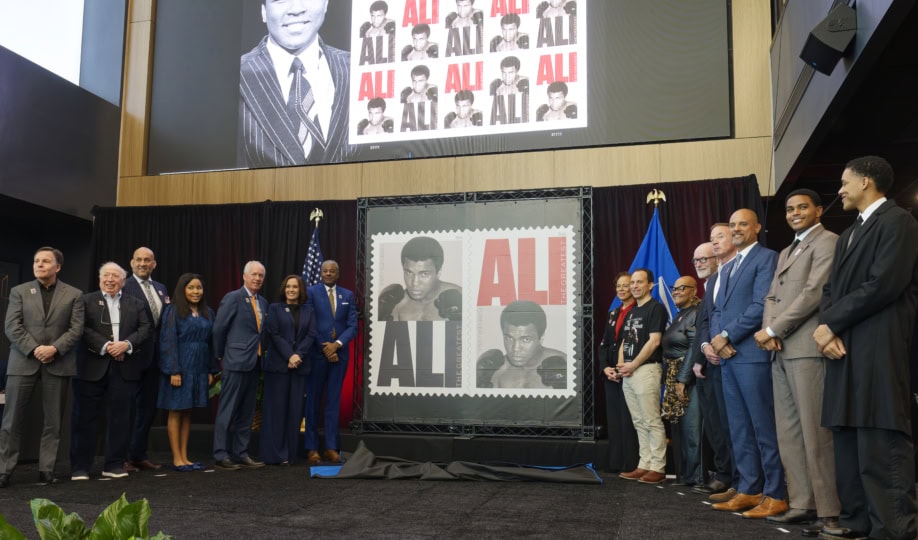 Group of people on stage in front of display showcasing the Muhammad Ali Forever stamps