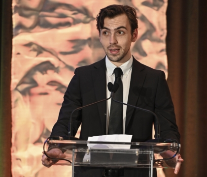 Man in black suit and tie speaking at lecturn
