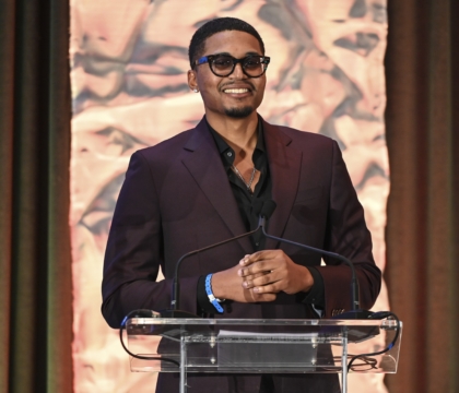 Man with dark purple jacket and black glasses speaks at lecturn