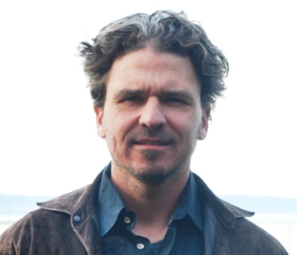Man wearing brown denim jacket and blue button-up shirt poses for camera