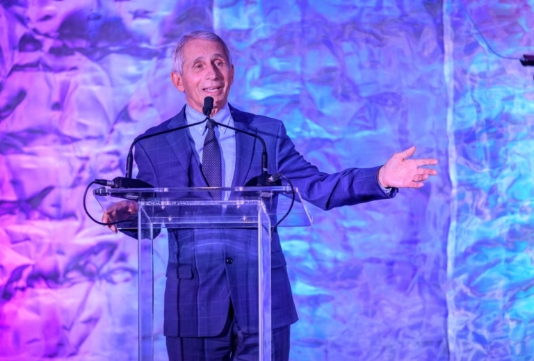 Dr. Fauci in a suit speaking at a lectern