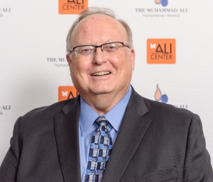 Man with glasses wearing jacket with blue shirt and tie poses for camera