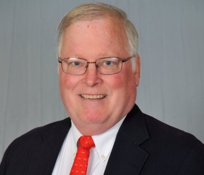 Man with glasses wearing black jacket, white shirt and red tie smiles at camera