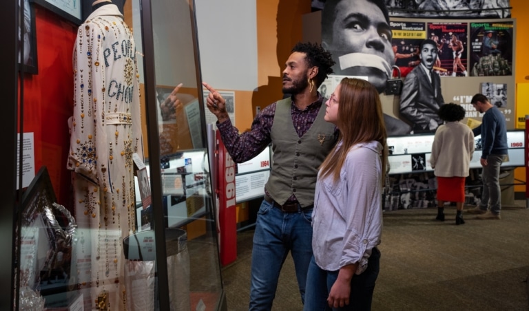 Two people in an exhibit hall pointing at a jumpsuit inside a case