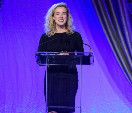 Woman with black dress smiles and speaks at lecturn