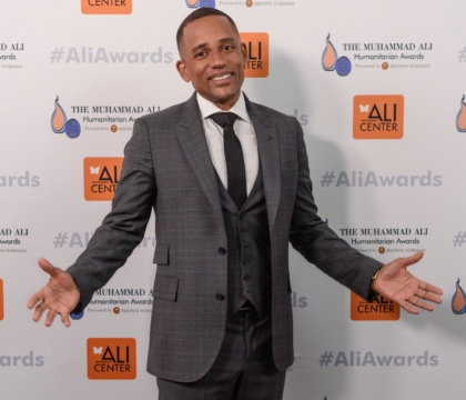 Man with gray suit, black vest and black tie poses for camera with arms out
