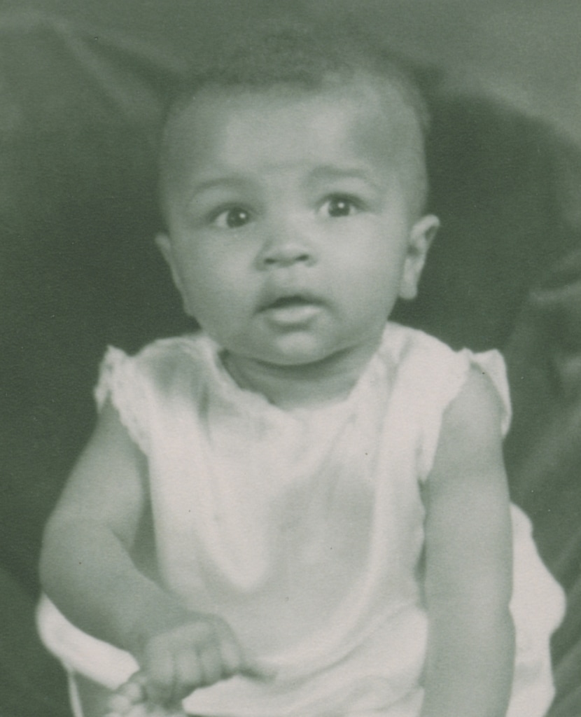 Black and white photo of baby Muhammad Ali (then Cassius Clay, Jr.) in white outfit