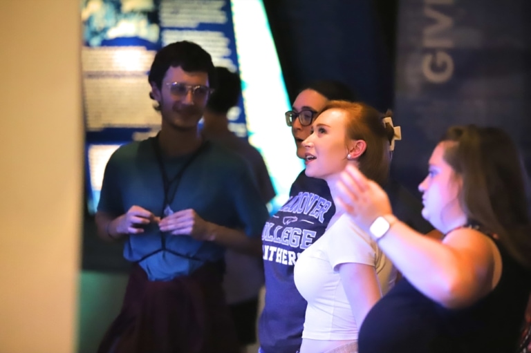 A group of four students in a dark exhibit gallery