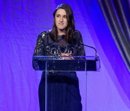 Woman wearing dark-colored suit with silver designs speaks at lecturn