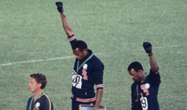Photo of three men on Olympic podium with two raising fists in the air