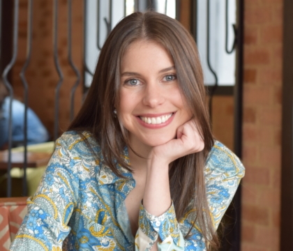 Woman wearing patterned blue shirt smiles for camera in coffee shop