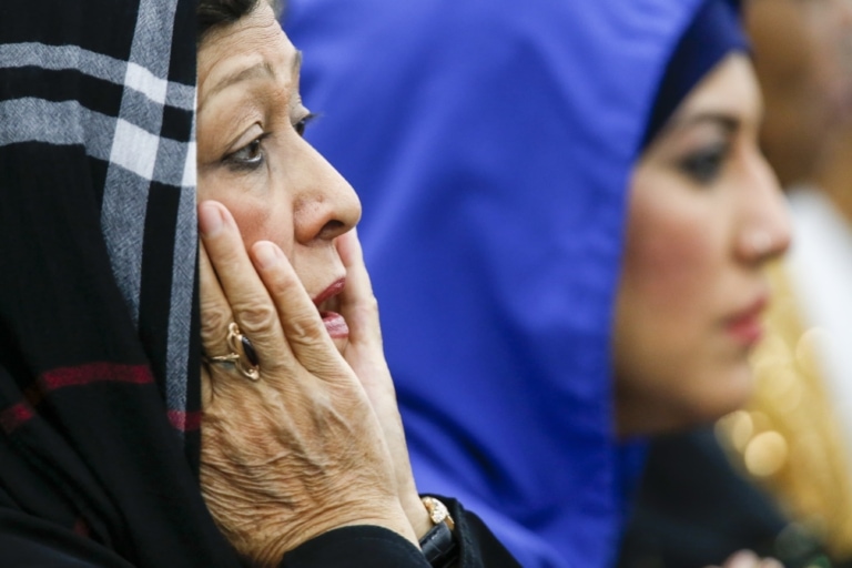 Women with head scarf sadly touches both sides of her face while observing something in the distance