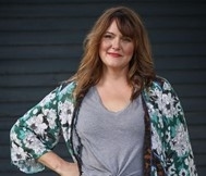 Woman in gray blouse and black pants with floral jacket posing for camera with arm on hip