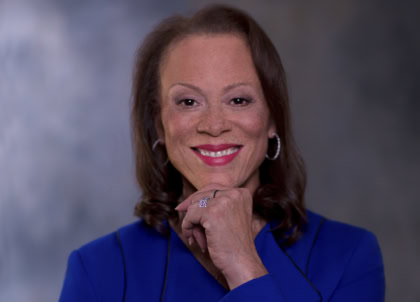 Woman with shoulder length dark hair wearing blue blazer smiling at camera