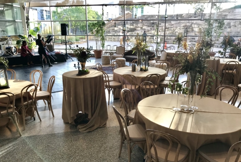 Room with a large glass wall and terrazzo flooring set up for an event with banquet round tables and chairs