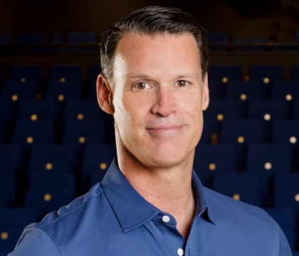 Man with blue button-up shirt posing for camera with dark background