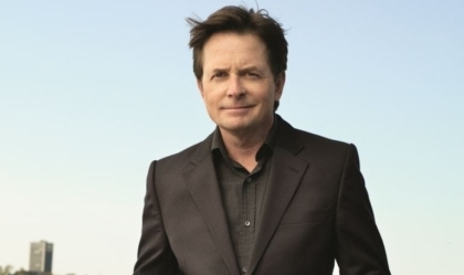 Michael J. Fox posing with black suit and black shirt in front of body of water