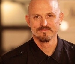 Man wearing black button-up shirt smiles for camera in front of blurry background
