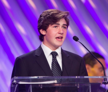 Man wearing black jacket, white shirt and black and white striped tie speaking at lecturn