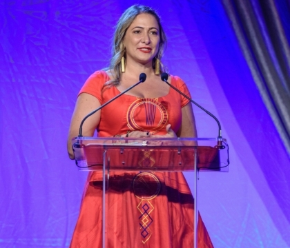 Woman wearing red dress with blue and gold patterns speaks at lecturn