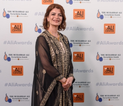 Woman wearing dark-colored dress with gold patterns poses for camera