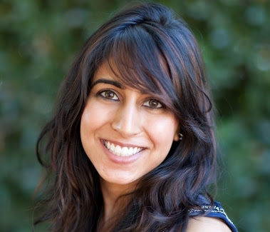 Woman wearing blue top smiles for camera in front of blurry green background