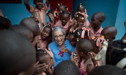 Woman wearing glasses and blue shirt smiles with group of children