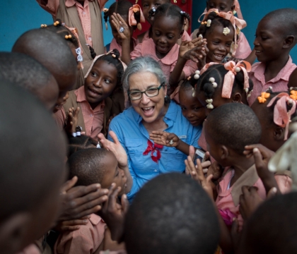 Woman wearing glasses and blue shirt smiles with group of children