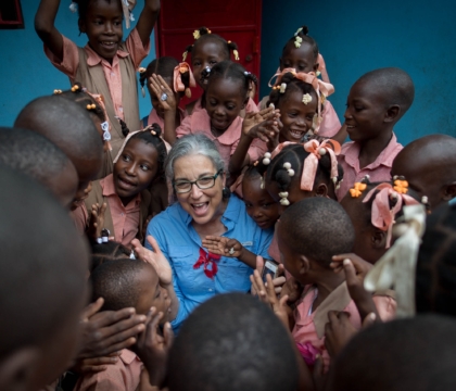 Woman wearing glasses and blue shirt smiles with group of children