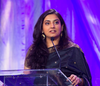 Woman wearing dark-colored dress speaking at lecturn