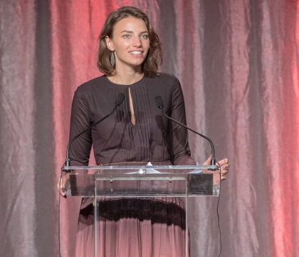 Woman wearing multi-colored dress smiles and speaks at lecturn