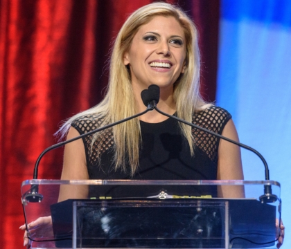 Woman wearing black dress smiles and speaks at lecturn
