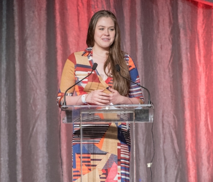 Woman wearing patterned dress with multiple colors speaks at lecturn