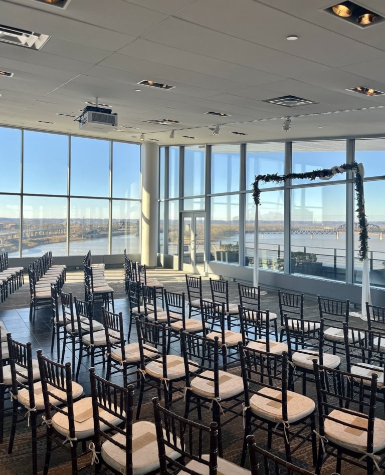 A wedding ceremony set up in a large room with large windows.