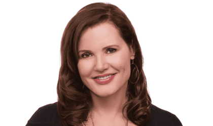 Geena Davis, wearing black top and gold necklace, smiles at camera