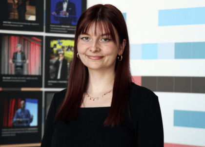 Woman with dark red hair wearing black top and jacket smiling at camera